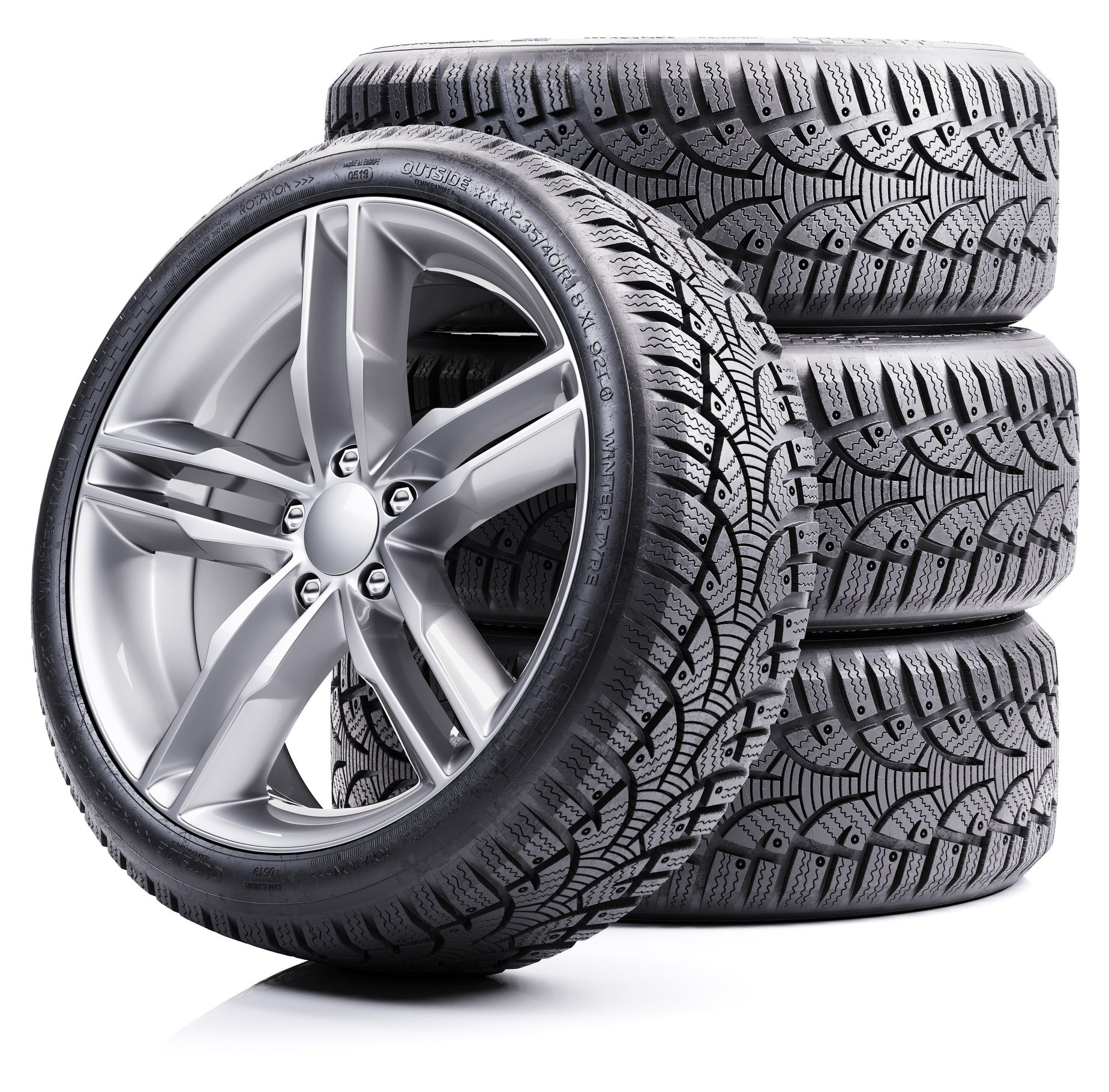 A silver-rimmed car wheel leaning against a stack of three black winter tires.
