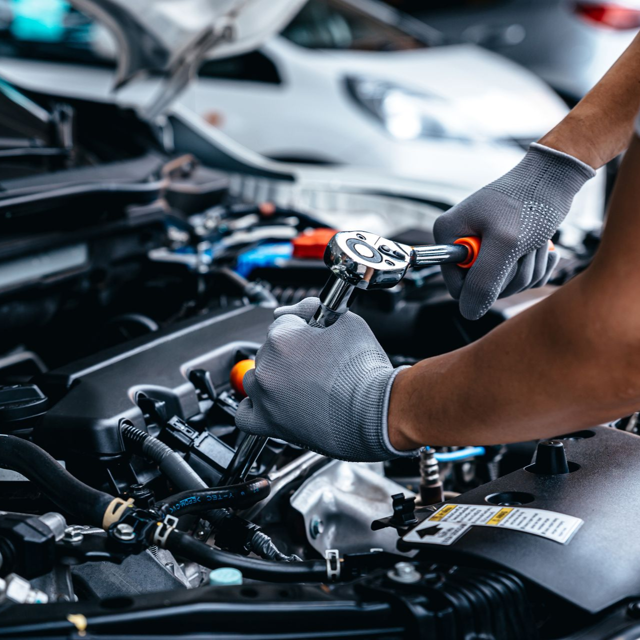 A person wearing grey work gloves uses a ratchet tool to perform maintenance on a car engine.
