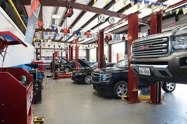 Interior of a vehicle repair shop featuring several cars in service bays, including a raised GMC truck and a sedan.