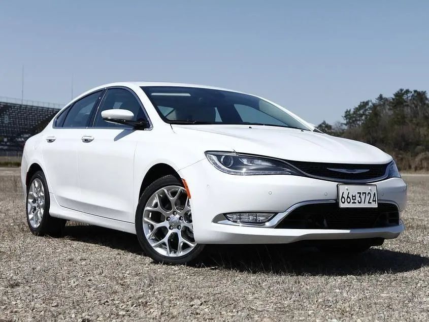A white Chrysler 200 sedan parked on a gravel surface under a clear blue sky.