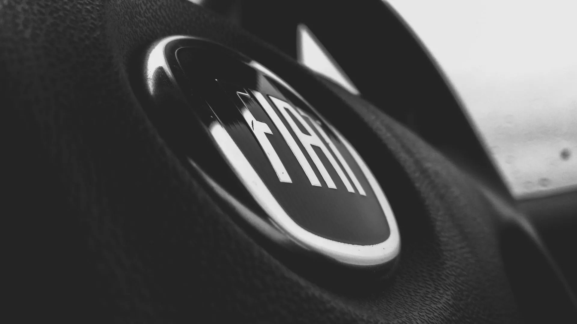 Close-up of a silver Fiat logo emblem centered on a black textured car steering wheel.
