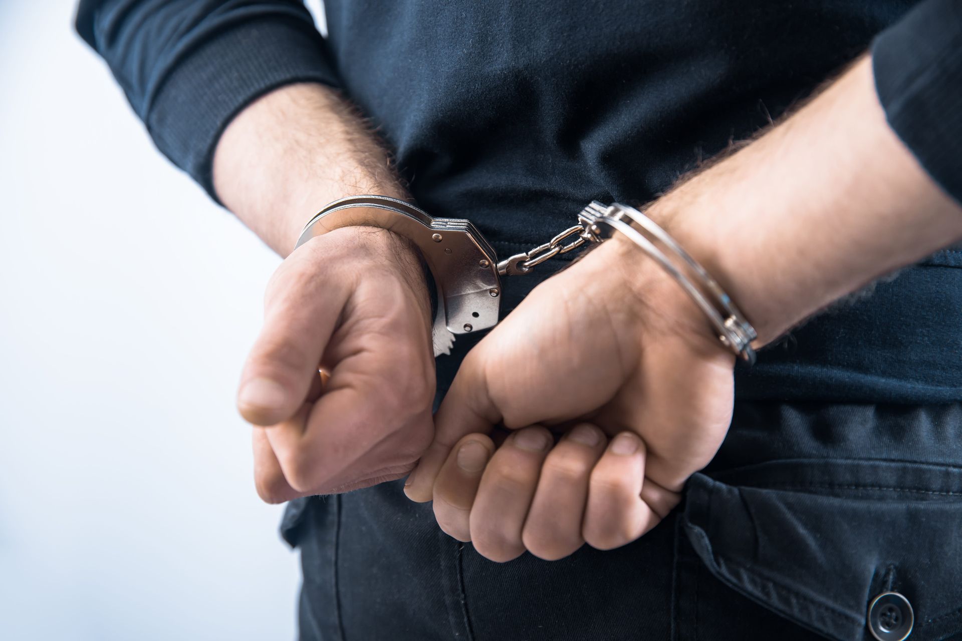 Handcuffed hands behind a person’s back in dark jeans and a black shirt