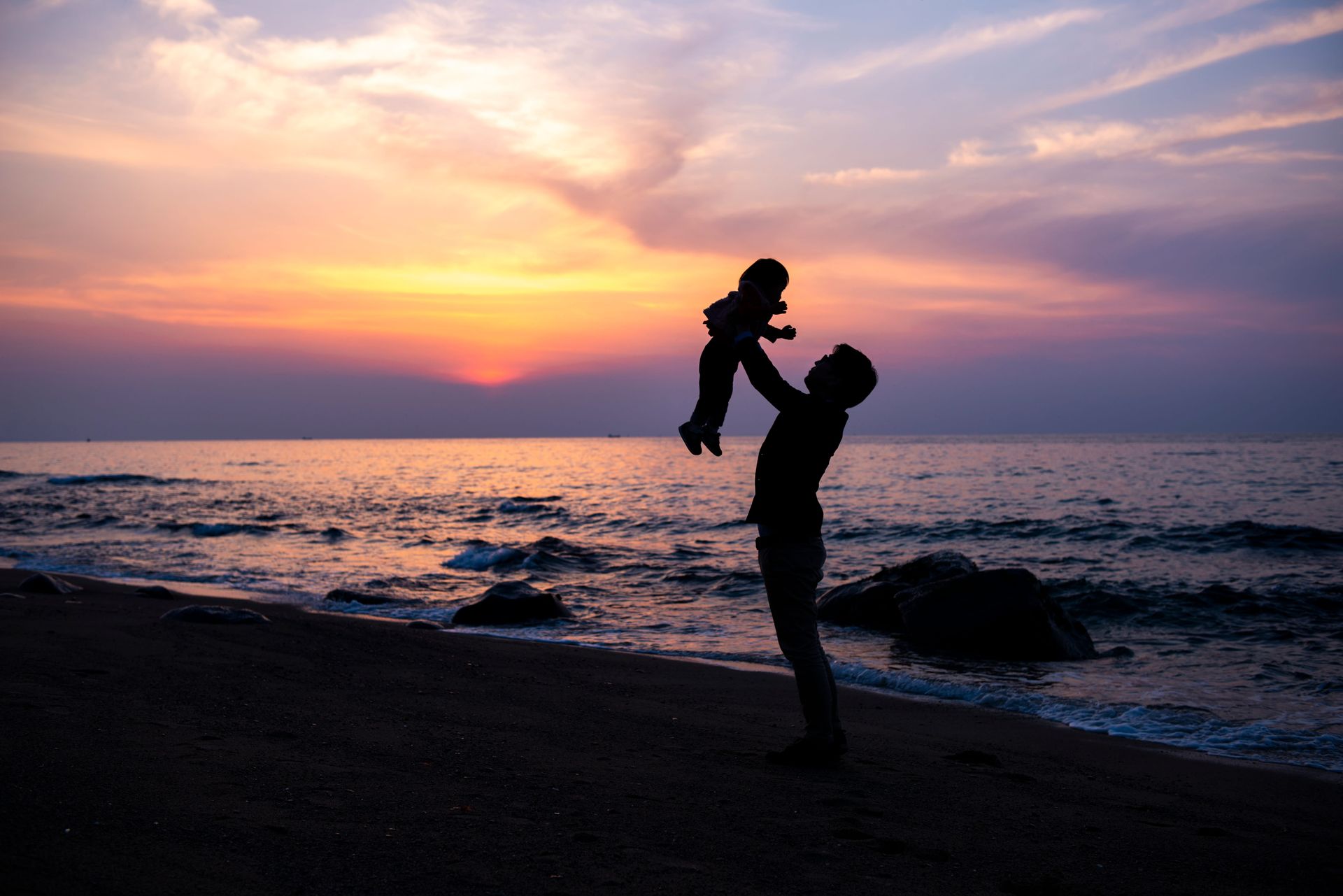 Silhouette of a person lifting a child at sunset on a beach by the ocean