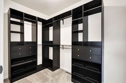 An empty walk-in closet with dark wood shelving, hanging rods, drawers, and open storage compartments on a carpeted floor.