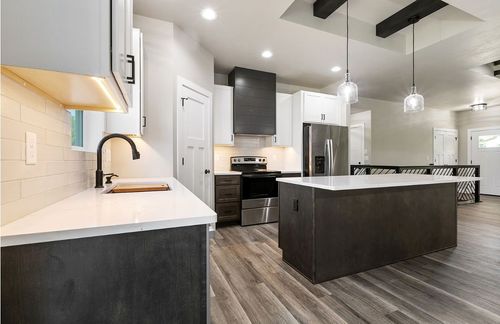 Modern kitchen with a dark-wood island, white countertops, stainless steel appliances, and wood-look flooring.