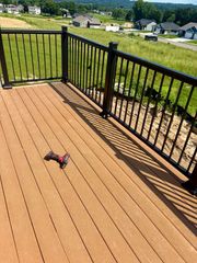 A red cordless drill sits on a light brown composite deck with black metal railings overlooking a residential area.