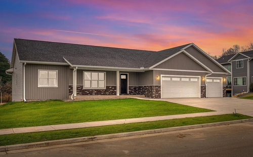 A single-story gray house with a stone foundation and a three-car garage under a vibrant sunset sky.