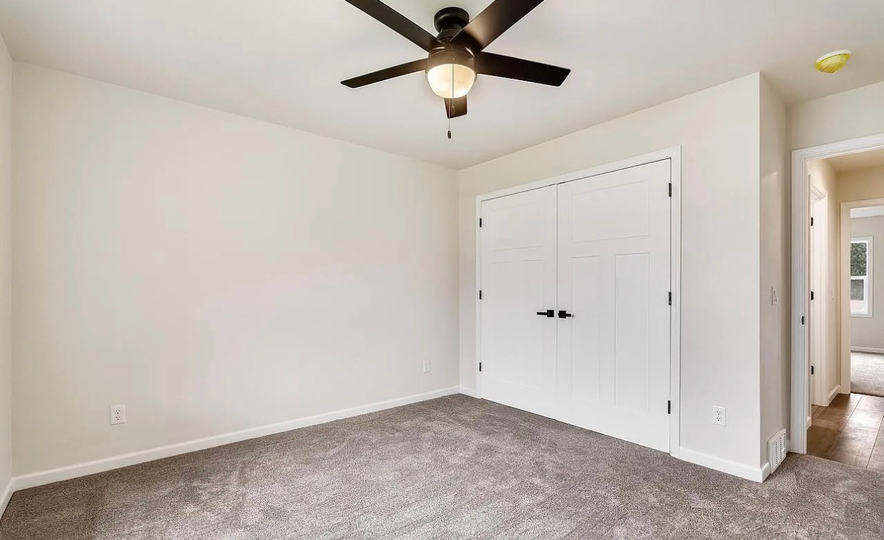 A neutral-colored bedroom featuring a ceiling fan, grey carpeting, and white double closet doors.
