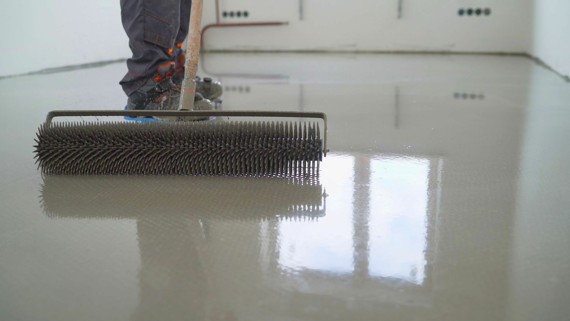 A person is using a broom to spread a concrete floor.