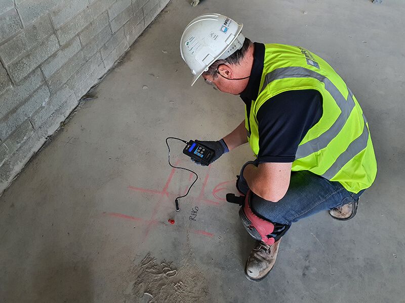 A man wearing a hard hat and a yellow vest is kneeling down on the floor.