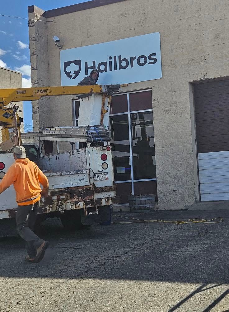 Worker in orange vest near a truck lift at a Hailbros building entrance