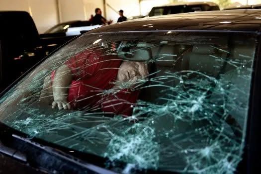 Person in red shirt behind shattered car windshield in a dim garage