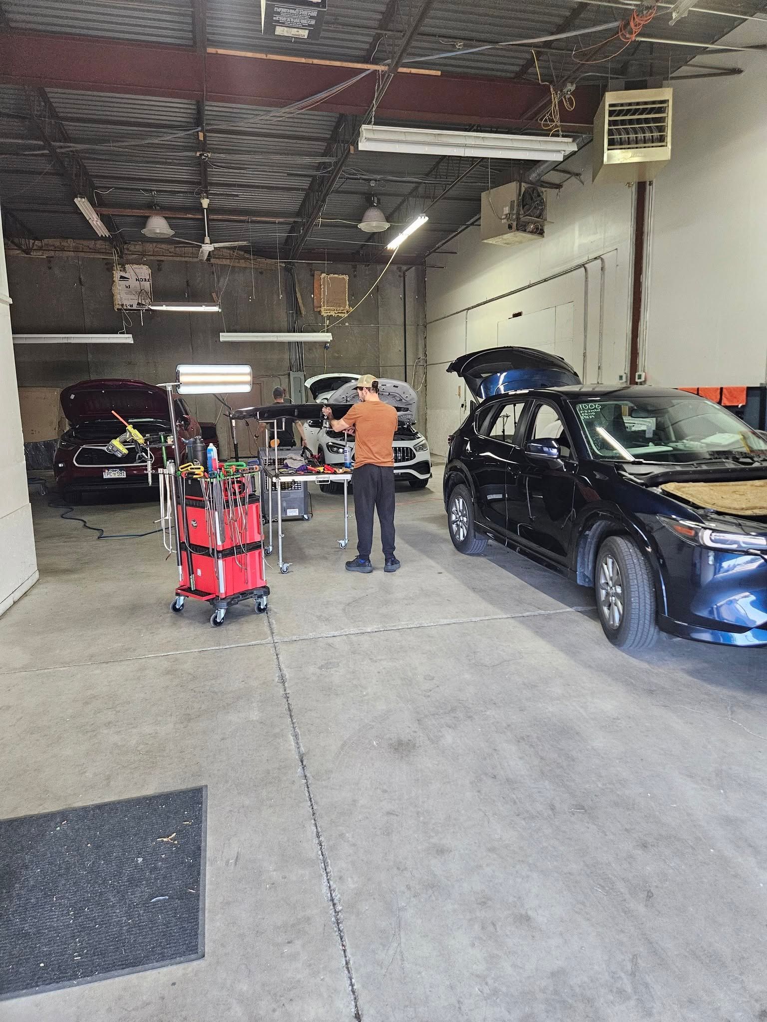 Auto repair shop with a black SUV, mechanic, and red tool cart inside a garage