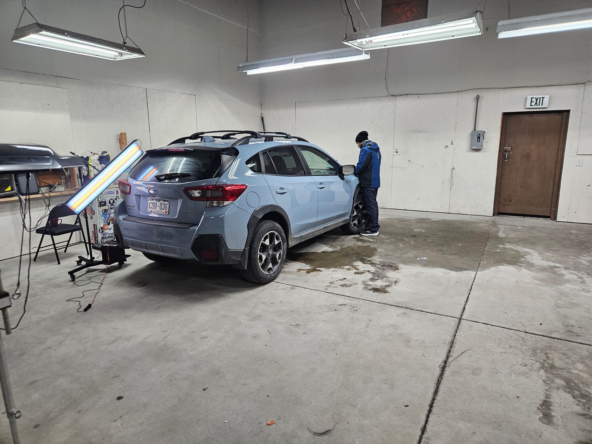 Person working on a light blue SUV in a garage with a paint easel nearby.