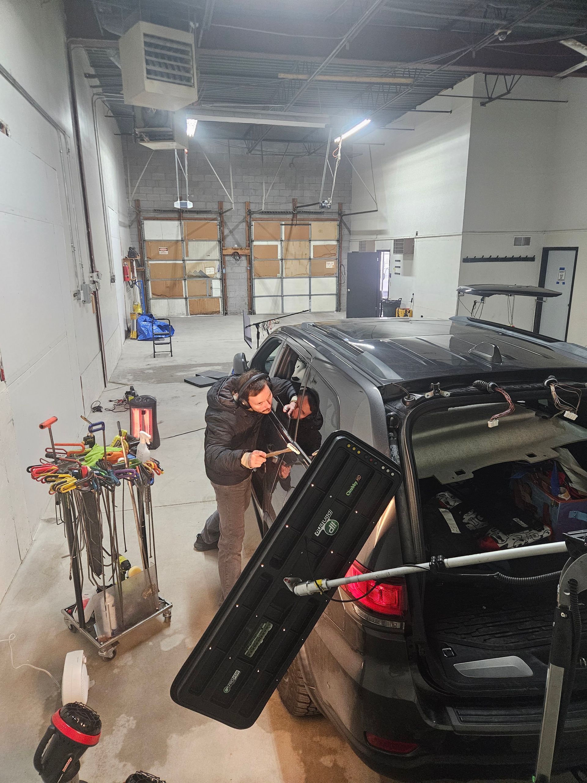 Person loading a black SUV in a warehouse garage, with shelves of boxes and tools nearby.