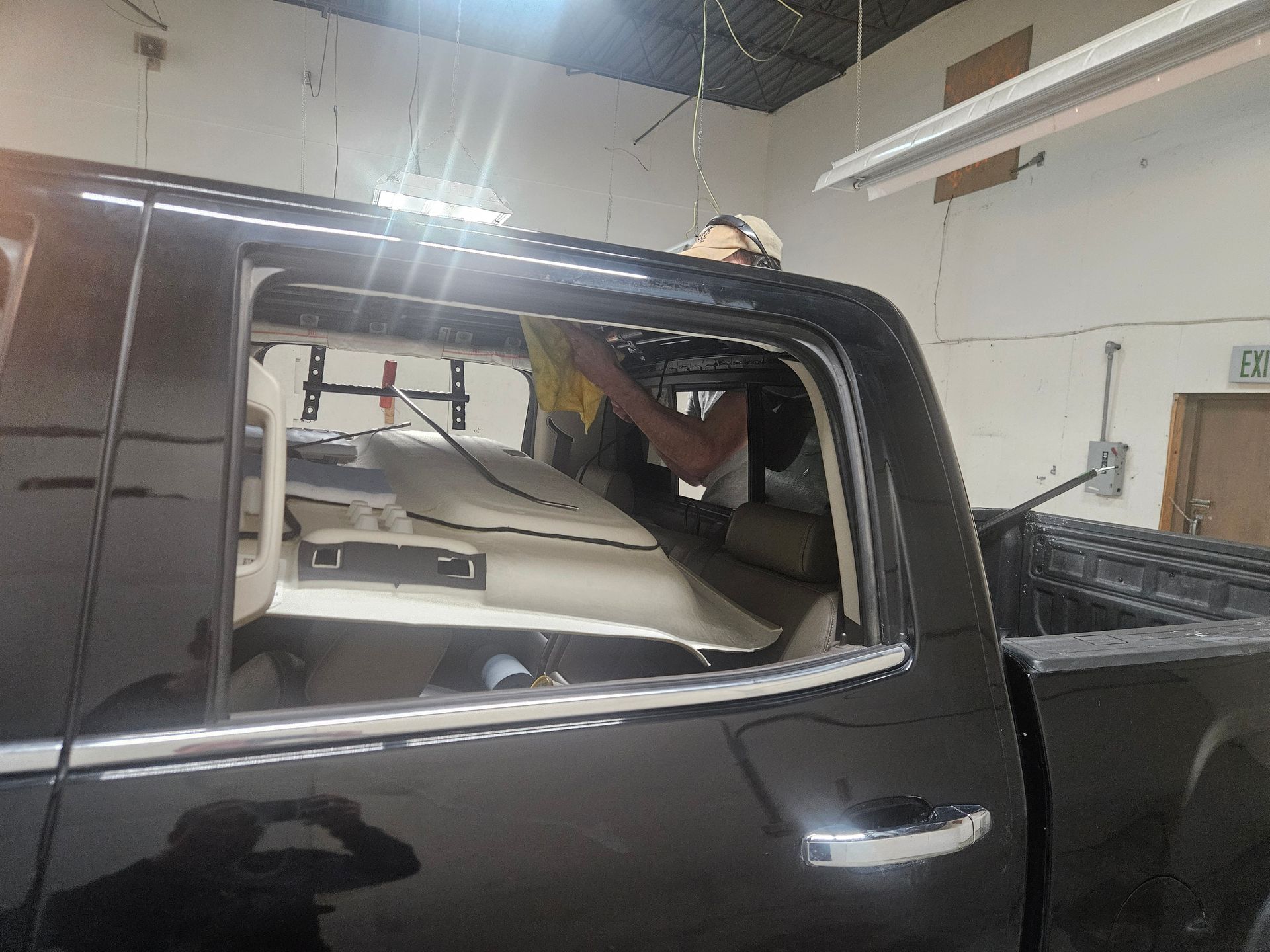 Black pickup truck with broken rear window inside a garage, with a person reaching through the opening