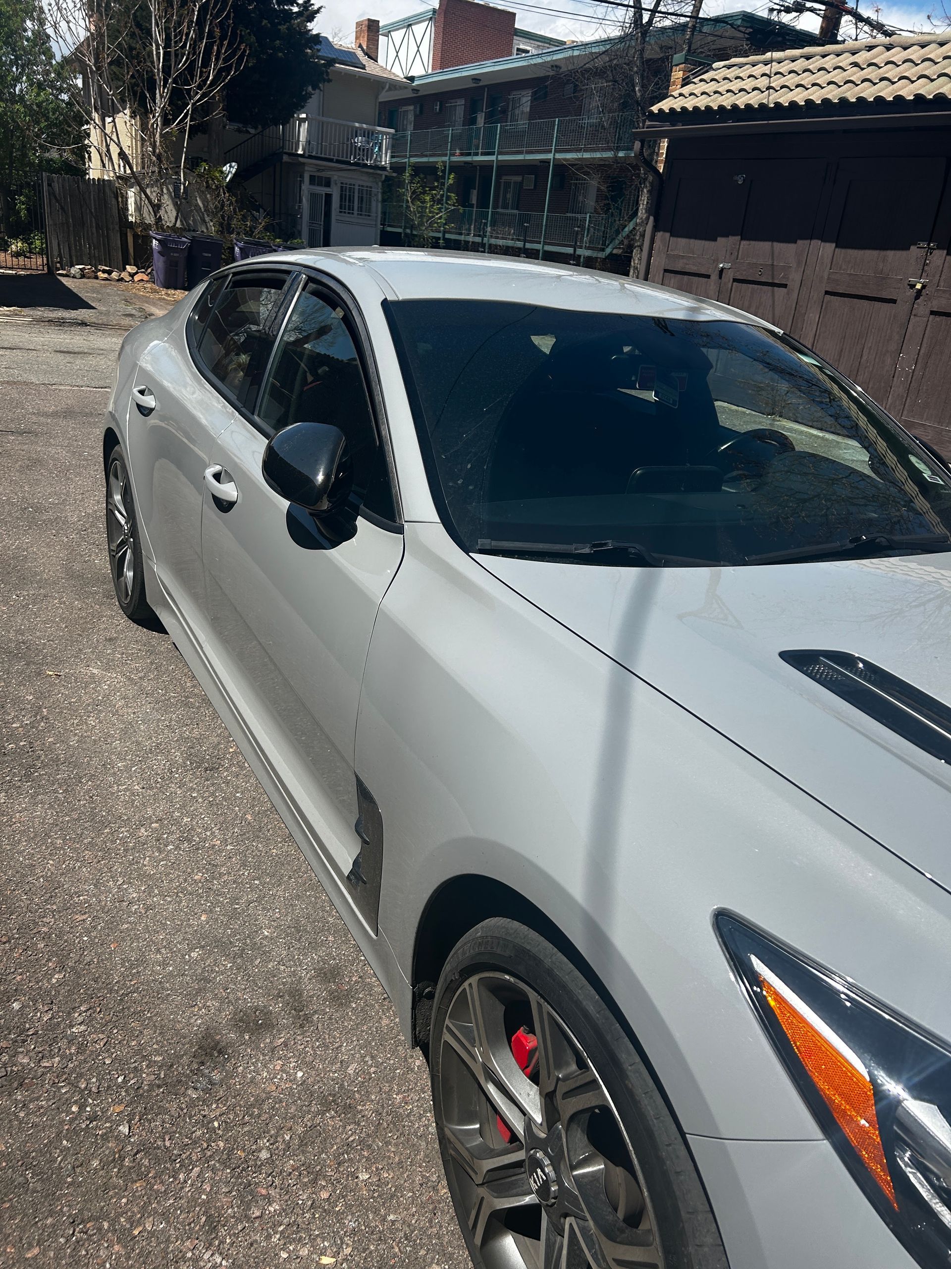 White sedan parked on a gravel driveway in front of a house, with red brake calipers visible