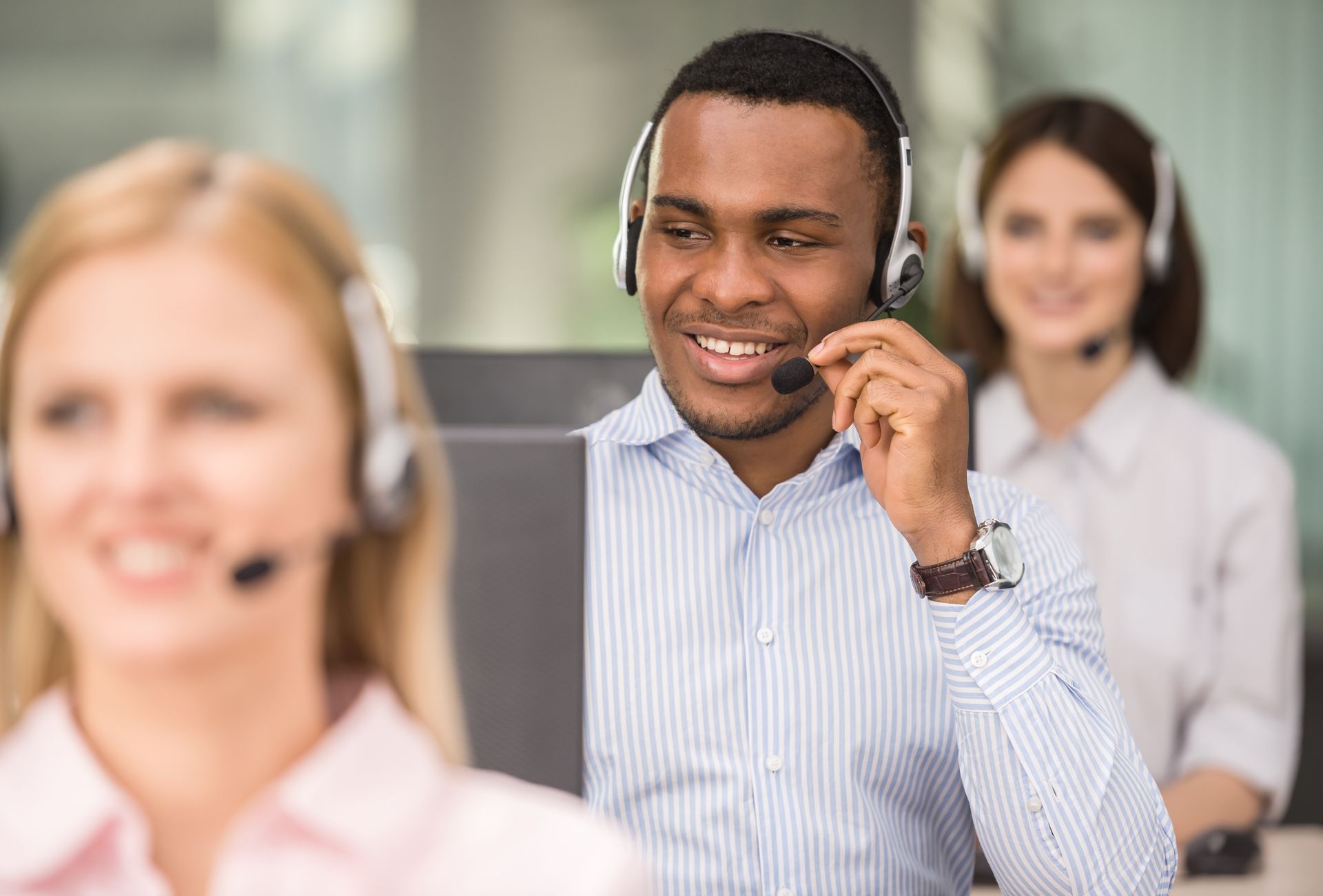 People in a call center wearing headsets; a Black man smiles while speaking into a microphone.