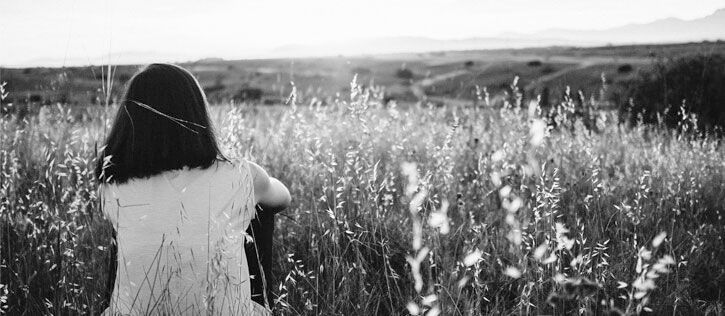 Young girl watching a sunset as she sits in a field of tall grass