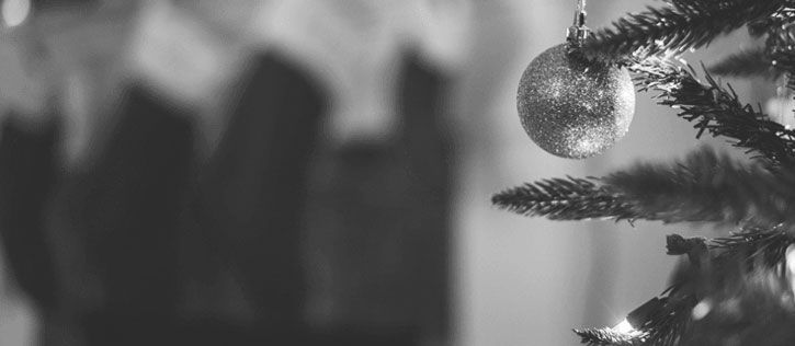 A solitary Christmas bauble hangs in front of a heavily blurred background of stockings, representing the loneliness of grief during the holidays