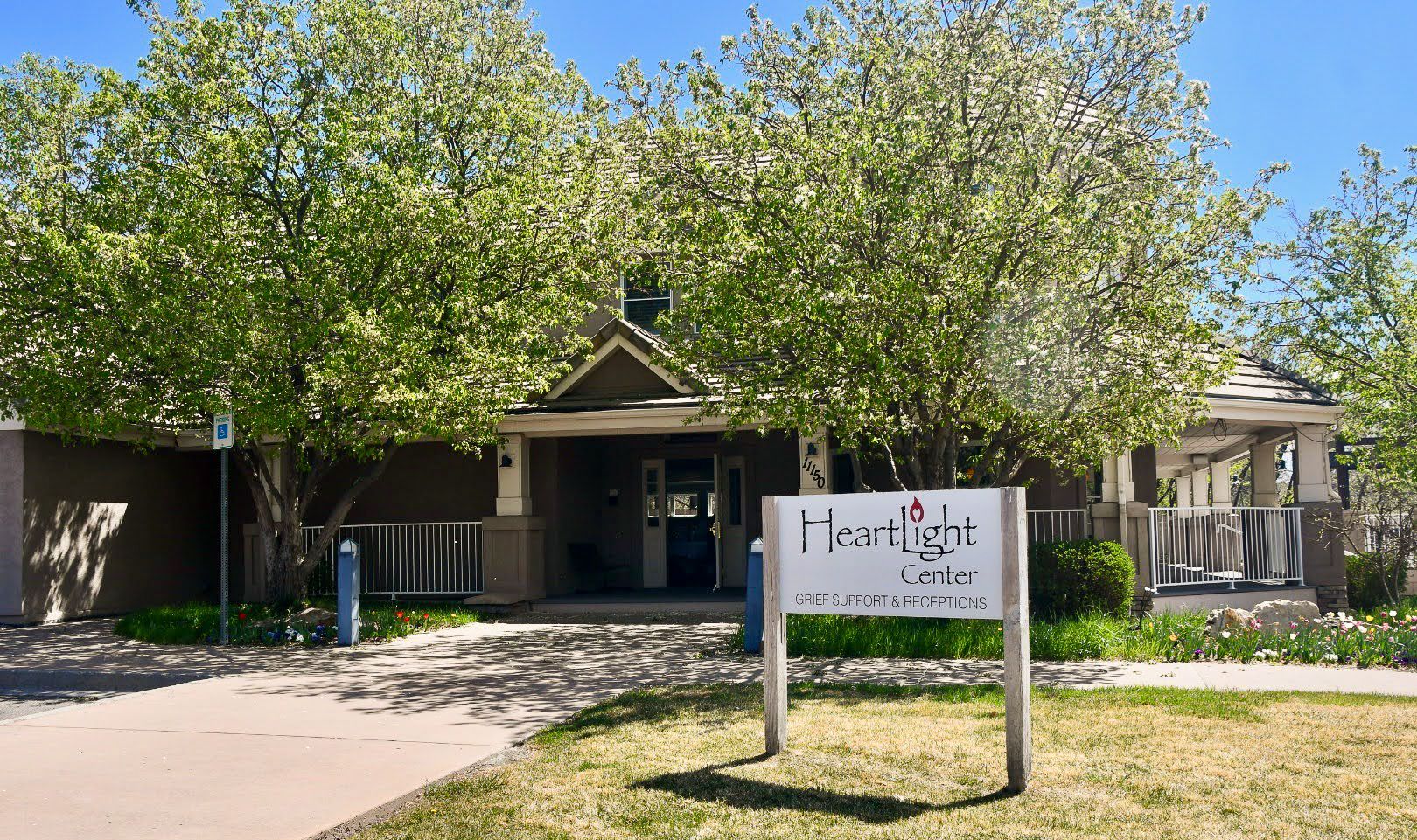 Front entrance of a building with a sign in front and trees shading the walkway