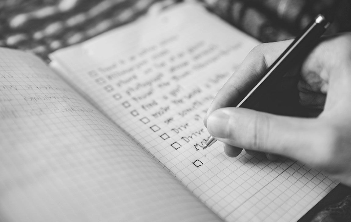 Black and white picture of someone writing a list to preplan a funeral.