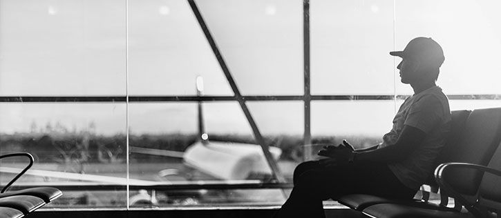 Young man traveling with cremains, sitting at an airport gate looking out a big glass window