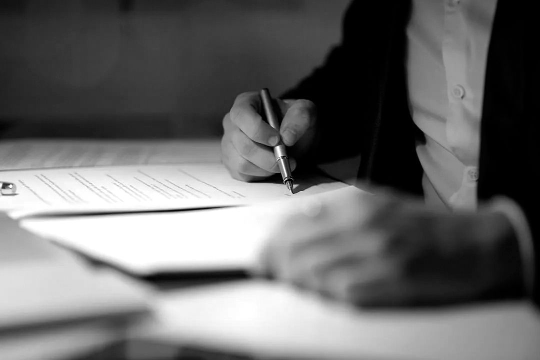 Person in a suit signing pre-planning funeral documents with a pen, preparing advance funeral arrangements and end-of-life planning checklist.