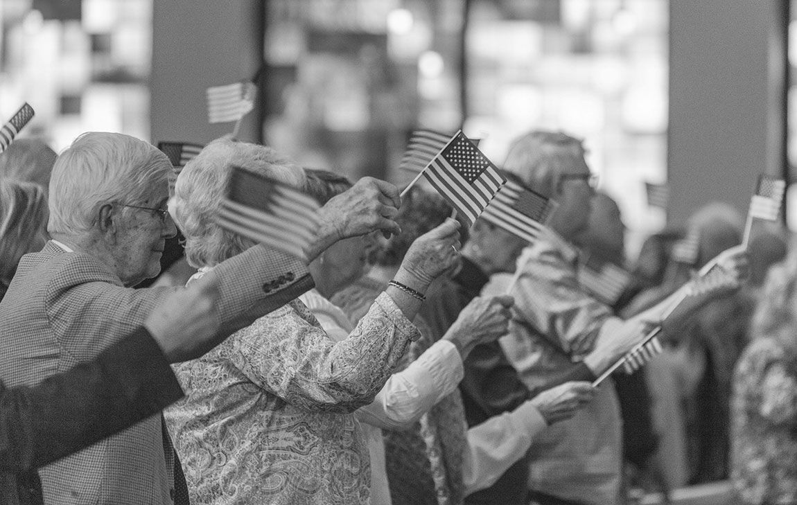 A group of men and women carrying small flags, assembled to honor veterans on Memorial Day