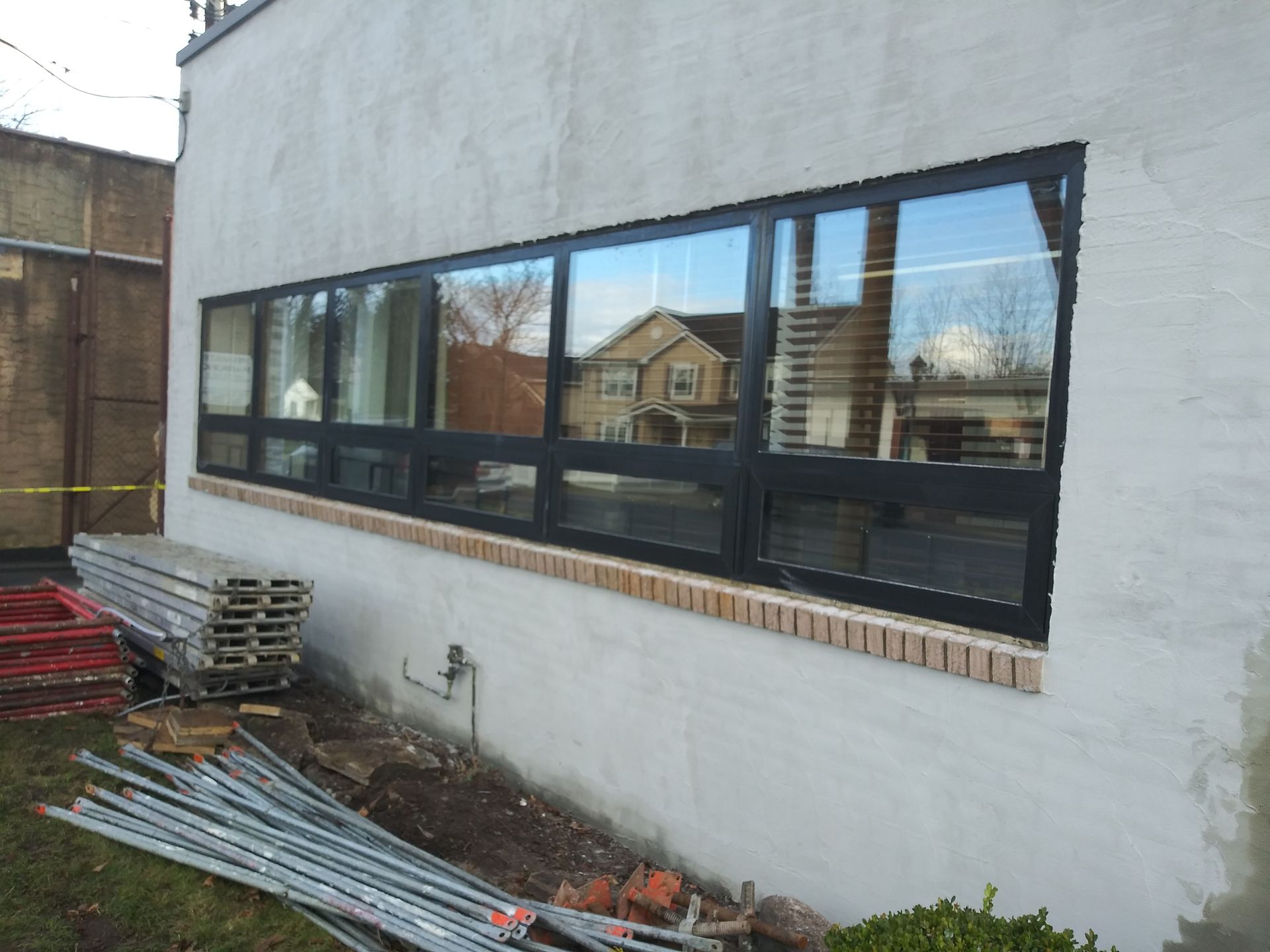 Exterior wall with a long row of black-framed windows at a construction site.
