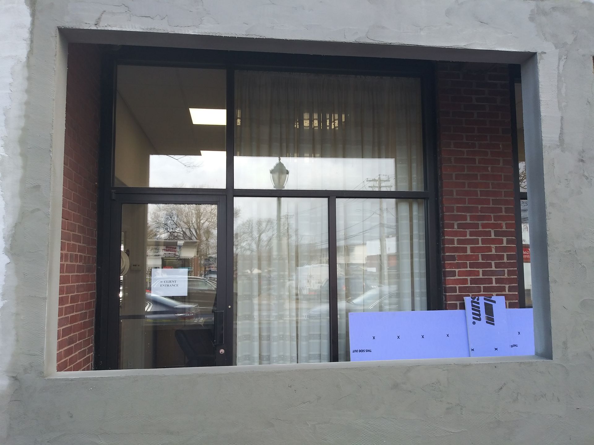 Storefront window with curtains, reflected street view, and blue signs in the lower right corner