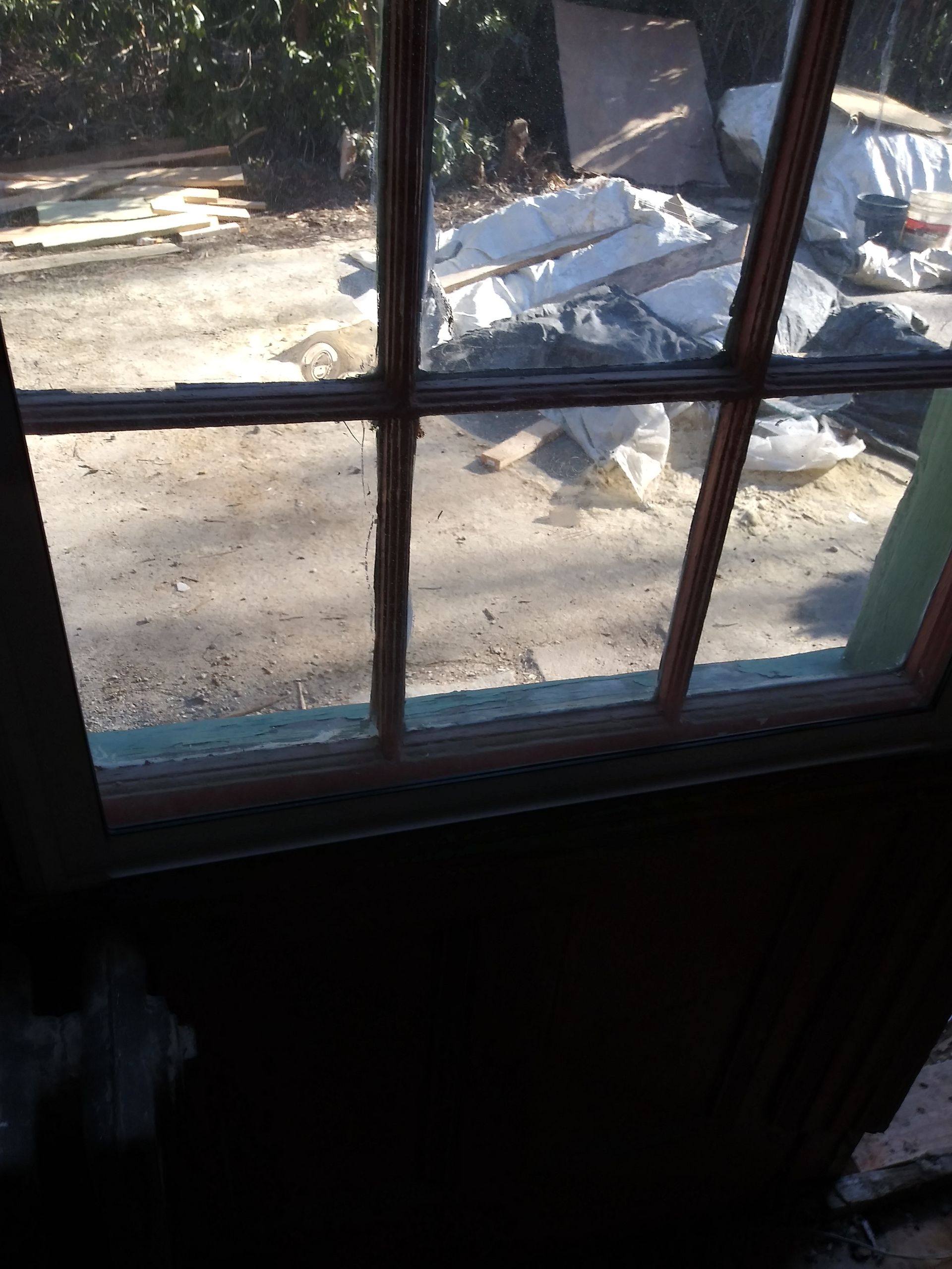 View through a window with wooden muntins, showing bright outdoor ground and a small snow pile.