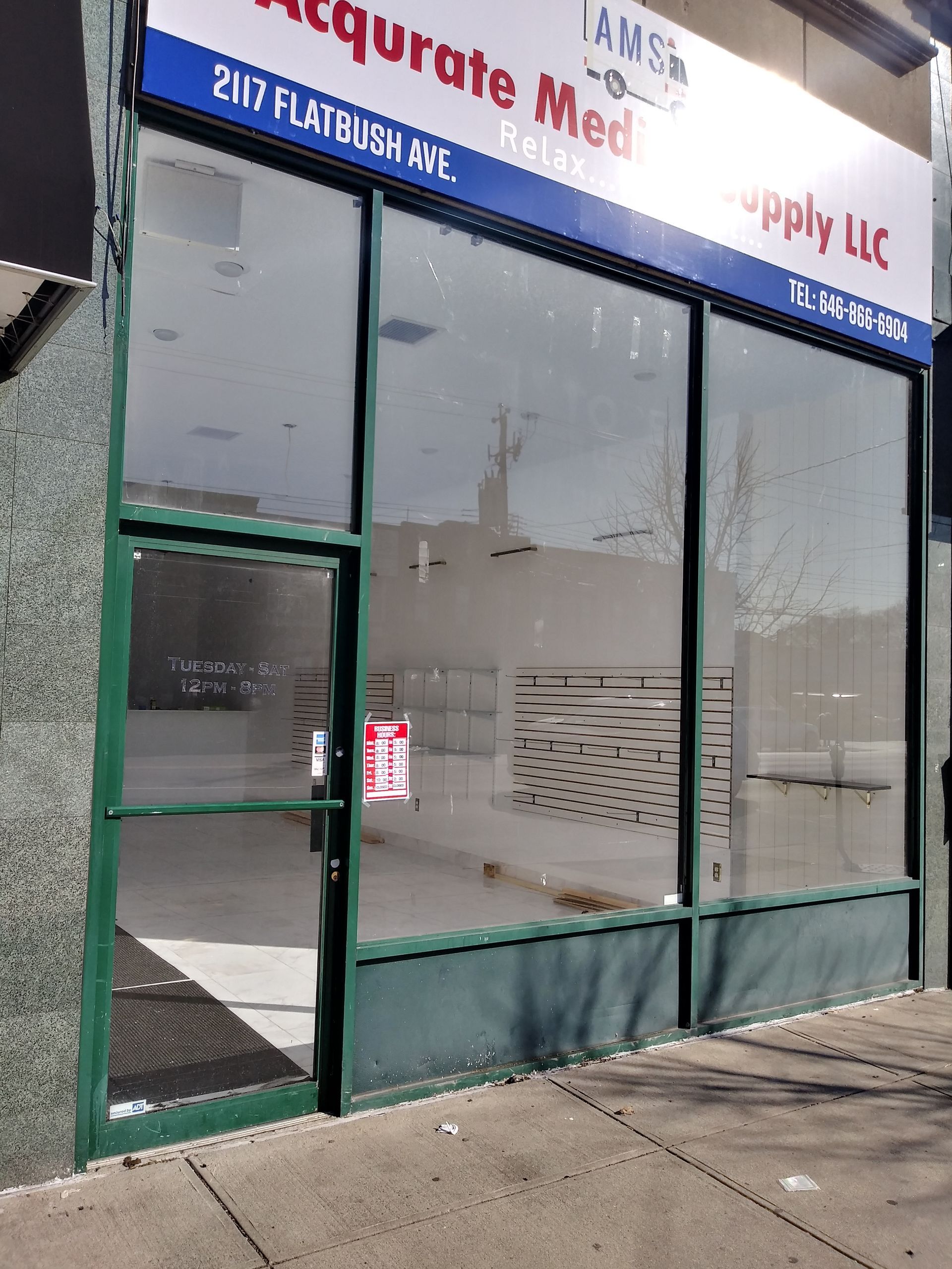 Glass storefront with green trim and a blue sign on a sidewalk