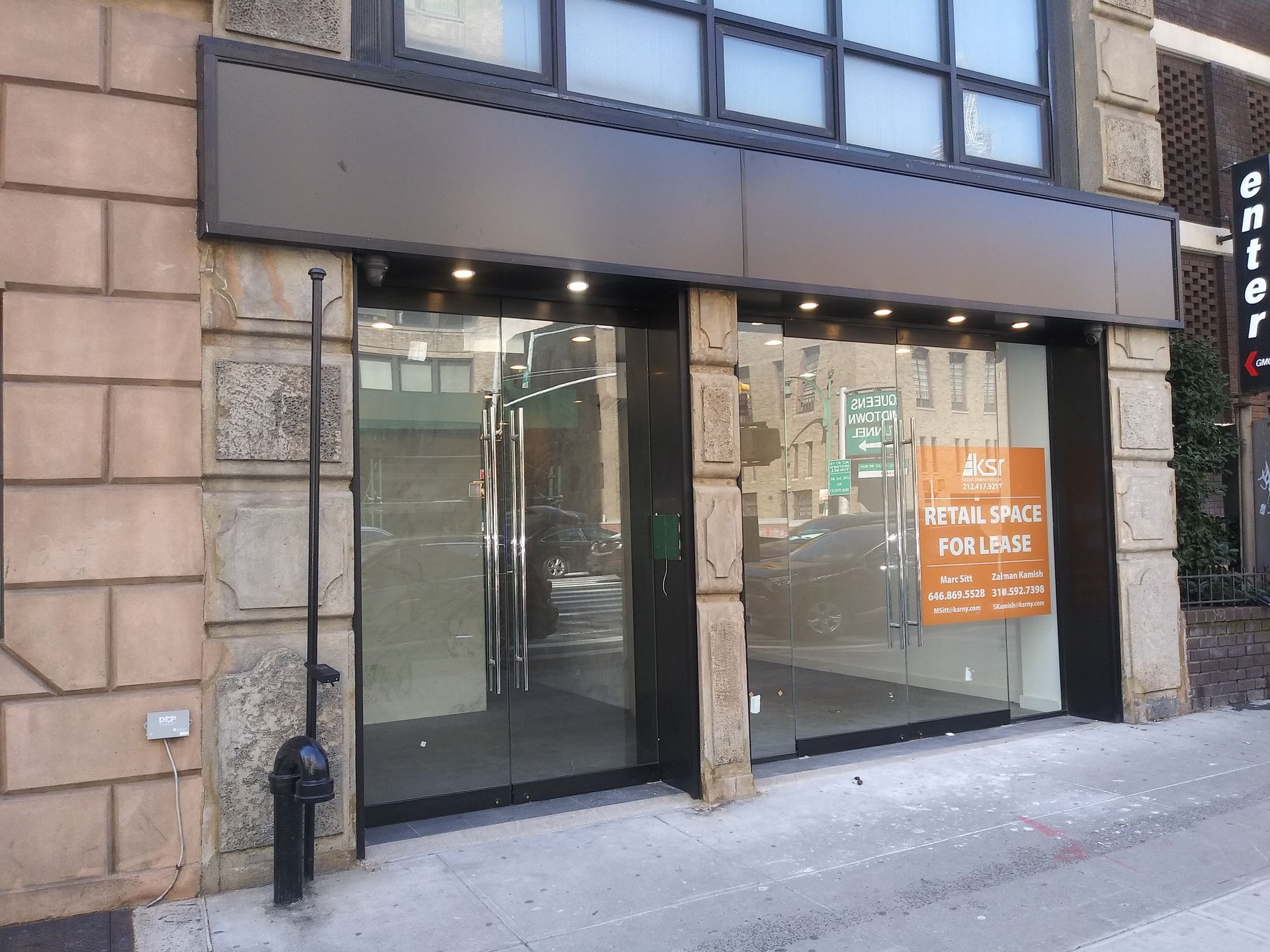 Storefront with glass entrance, stone facade, and an orange “please…” sign in the window.