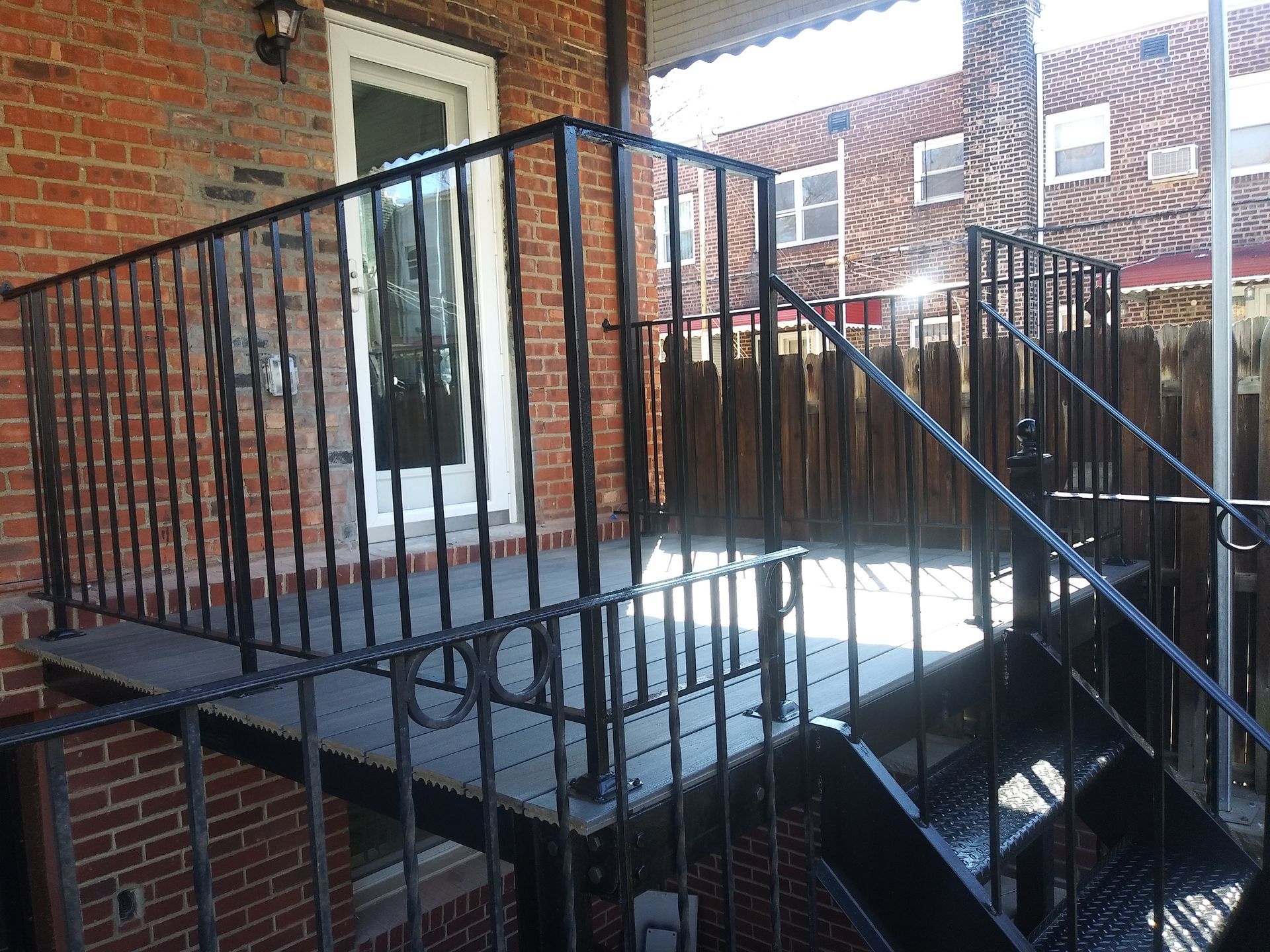 Black metal staircase and landing beside a brick building with white-trimmed door and windows