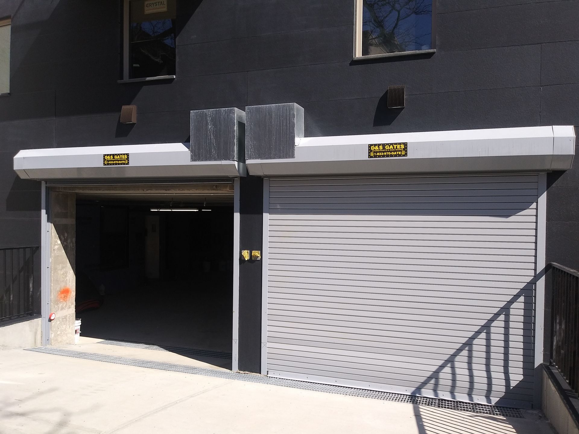 Two garage-style openings in a dark building facade, one open and one closed with a white roll-up door.