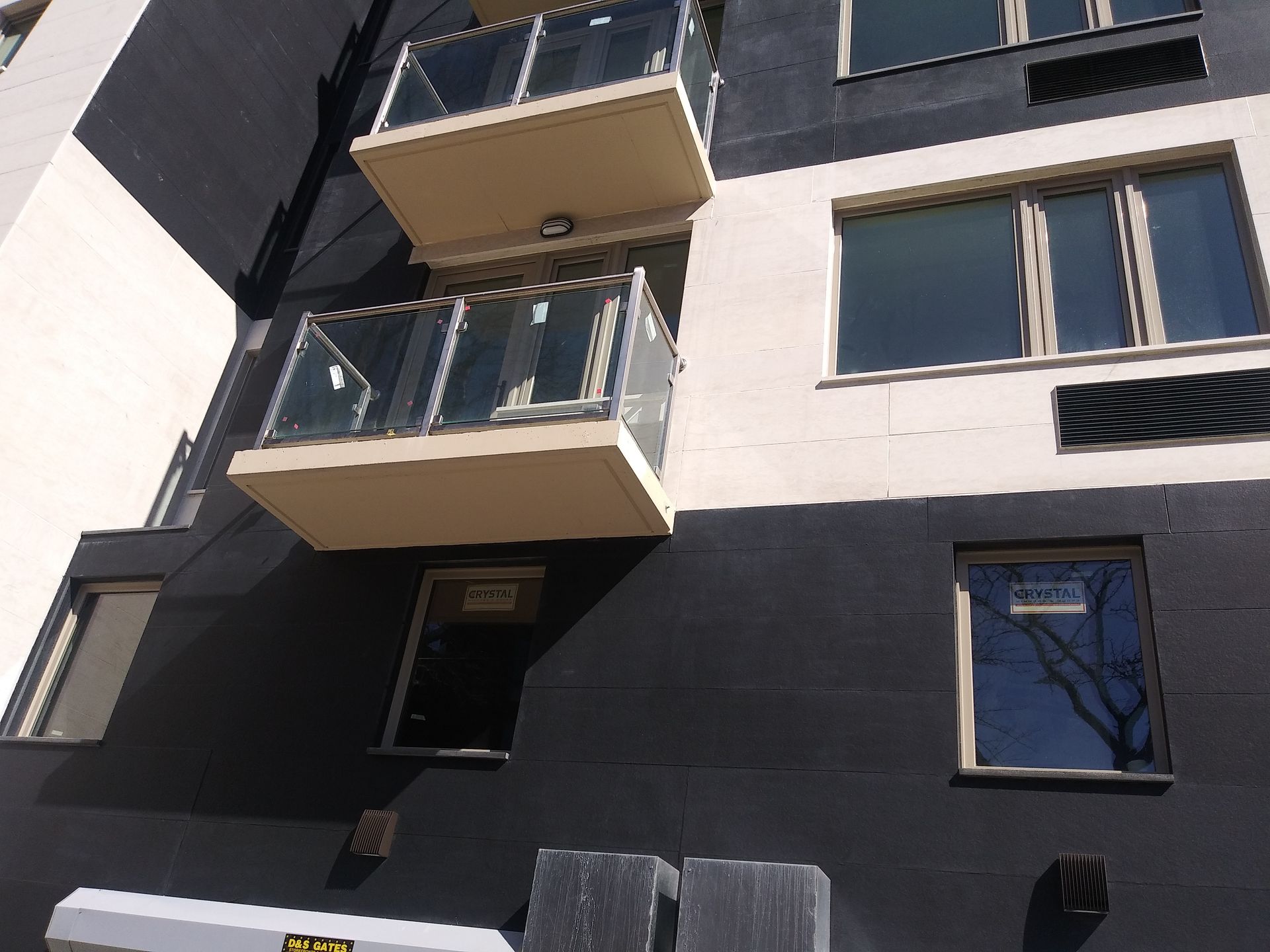 Modern apartment building facade with balconies, dark lower walls, and white upper walls in sunlight