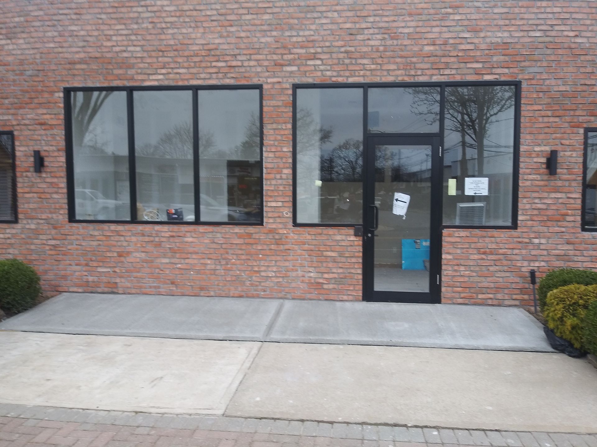 Brick storefront with large windows and glass door, showing an accessible entrance ramp.