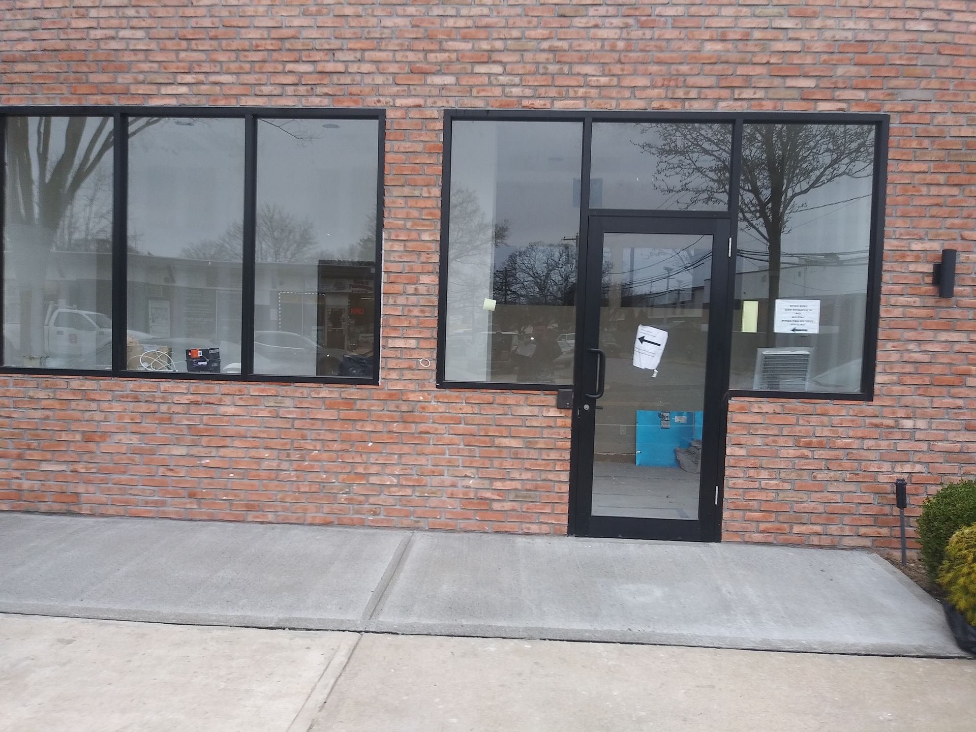 Brick storefront with two large windows and a glass door, viewed from the sidewalk.
