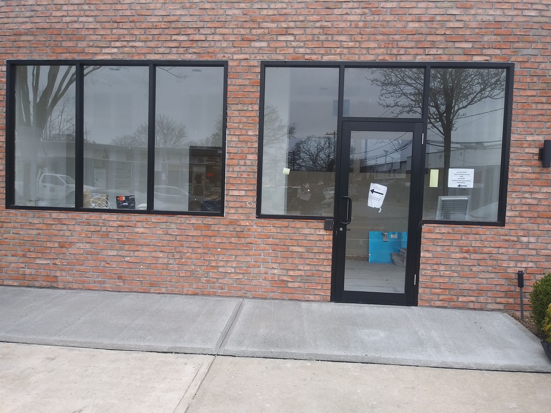 Brick storefront with large windows and a glass door, reflecting trees and sky.
