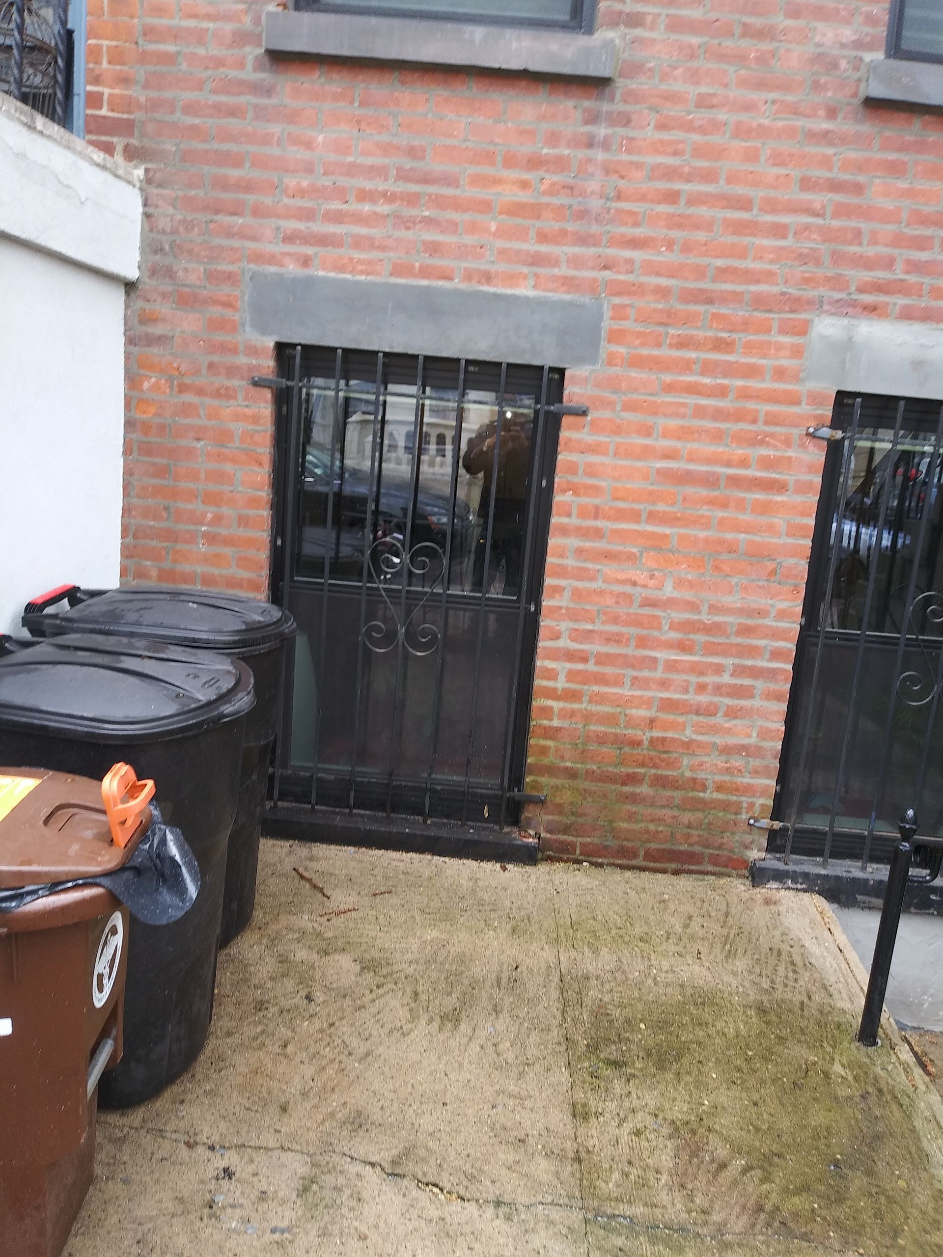 Brick building courtyard with two black metal doors, trash bins, and a wet concrete walkway.