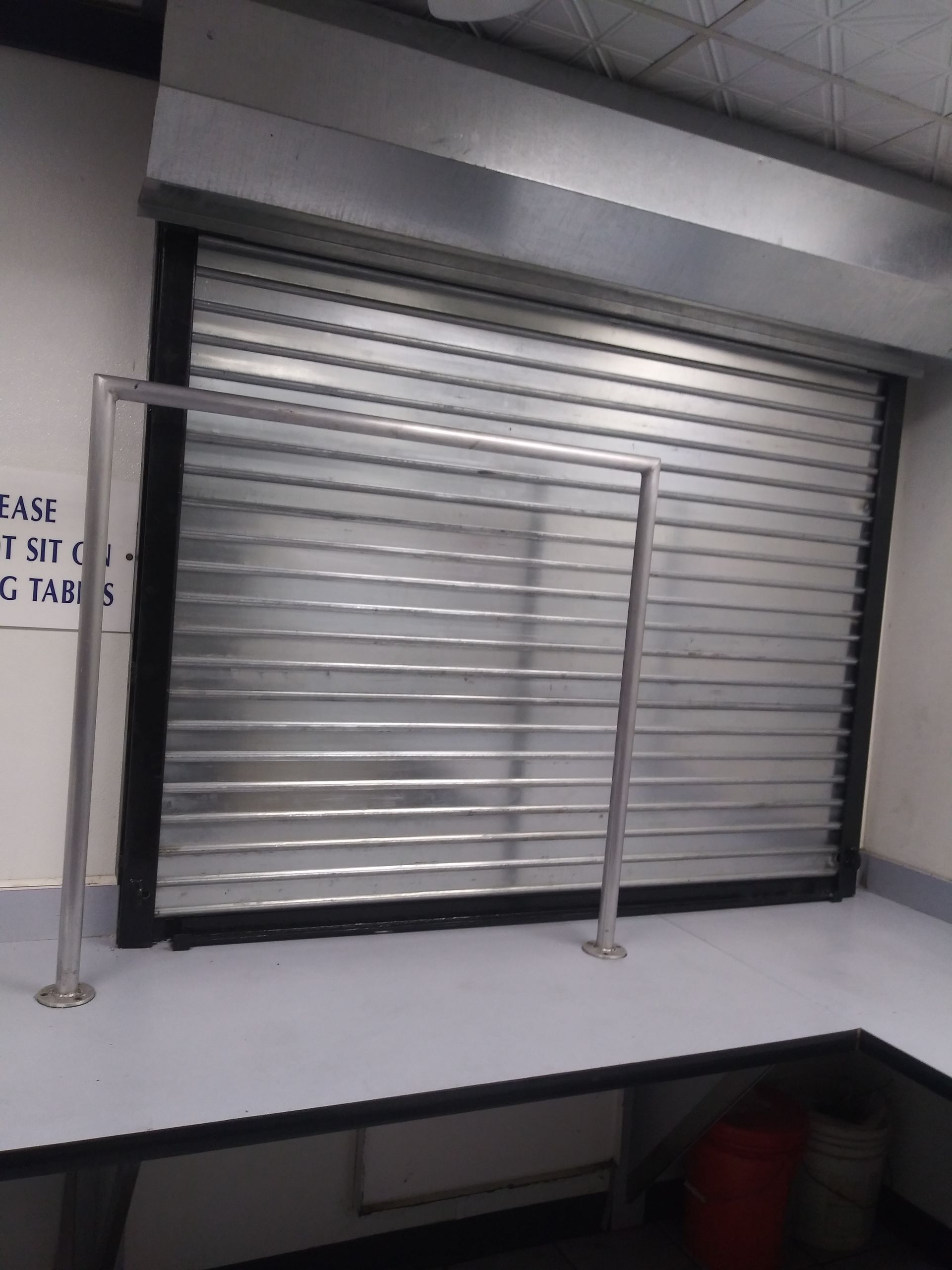Closed silver metal security shutter over a storefront window, with a black frame and support poles.