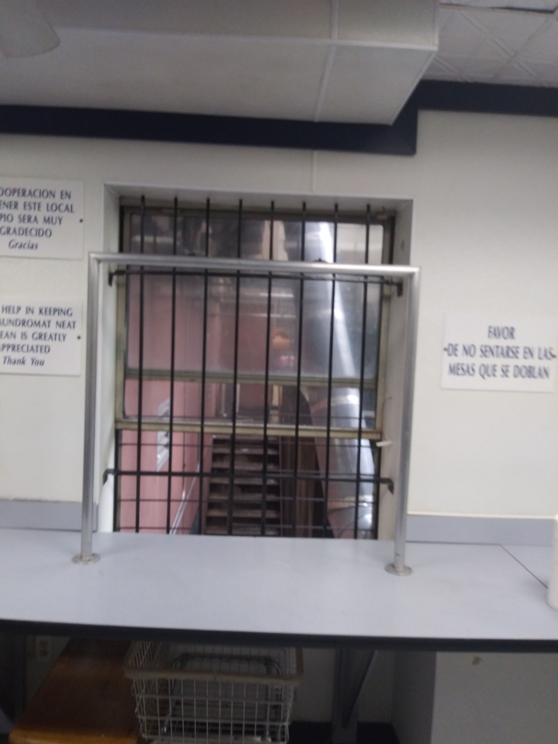 Closed barred window in a building interior, with signs on both sides and a desk in front.