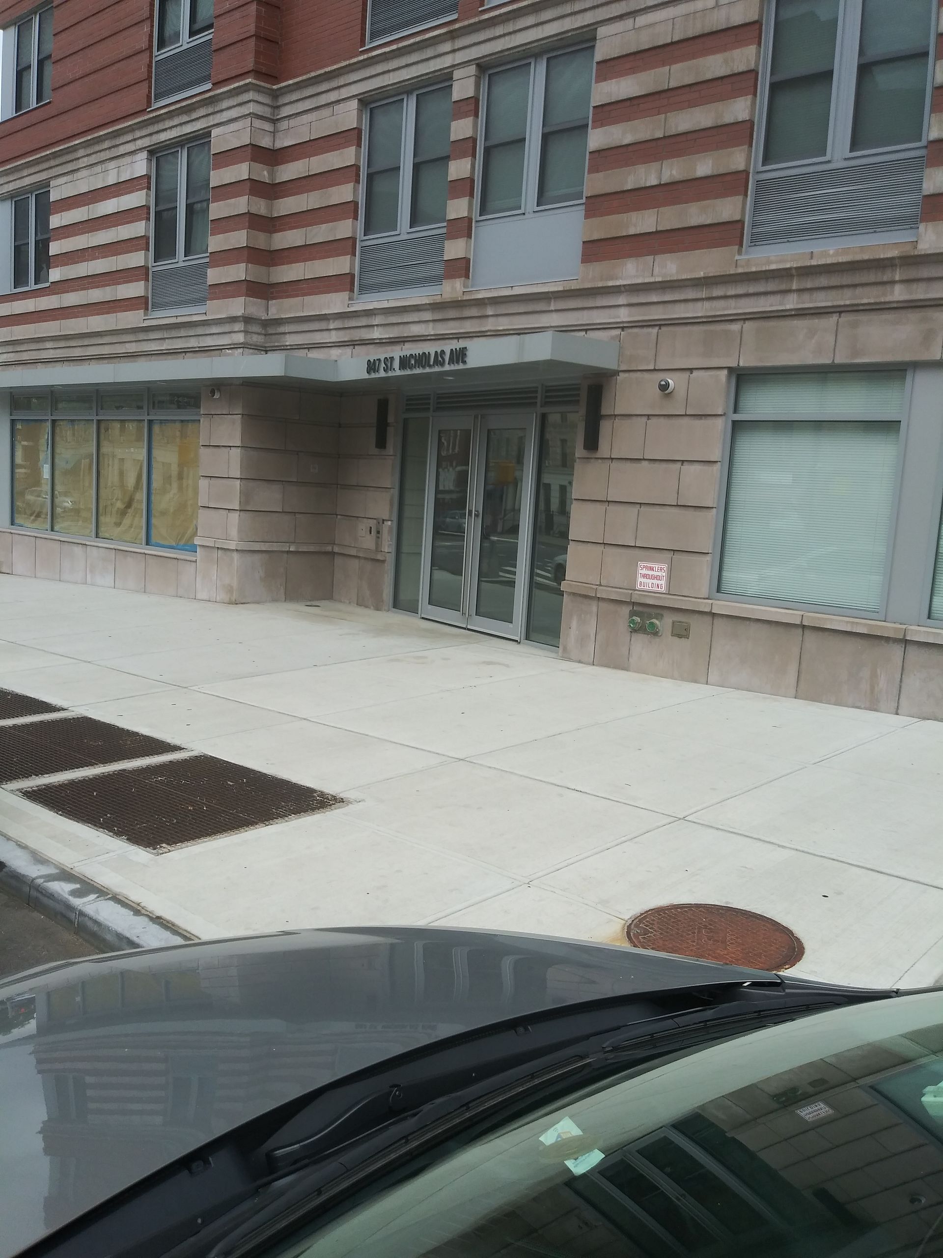Apartment building entrance on a city sidewalk, viewed from a parked car.