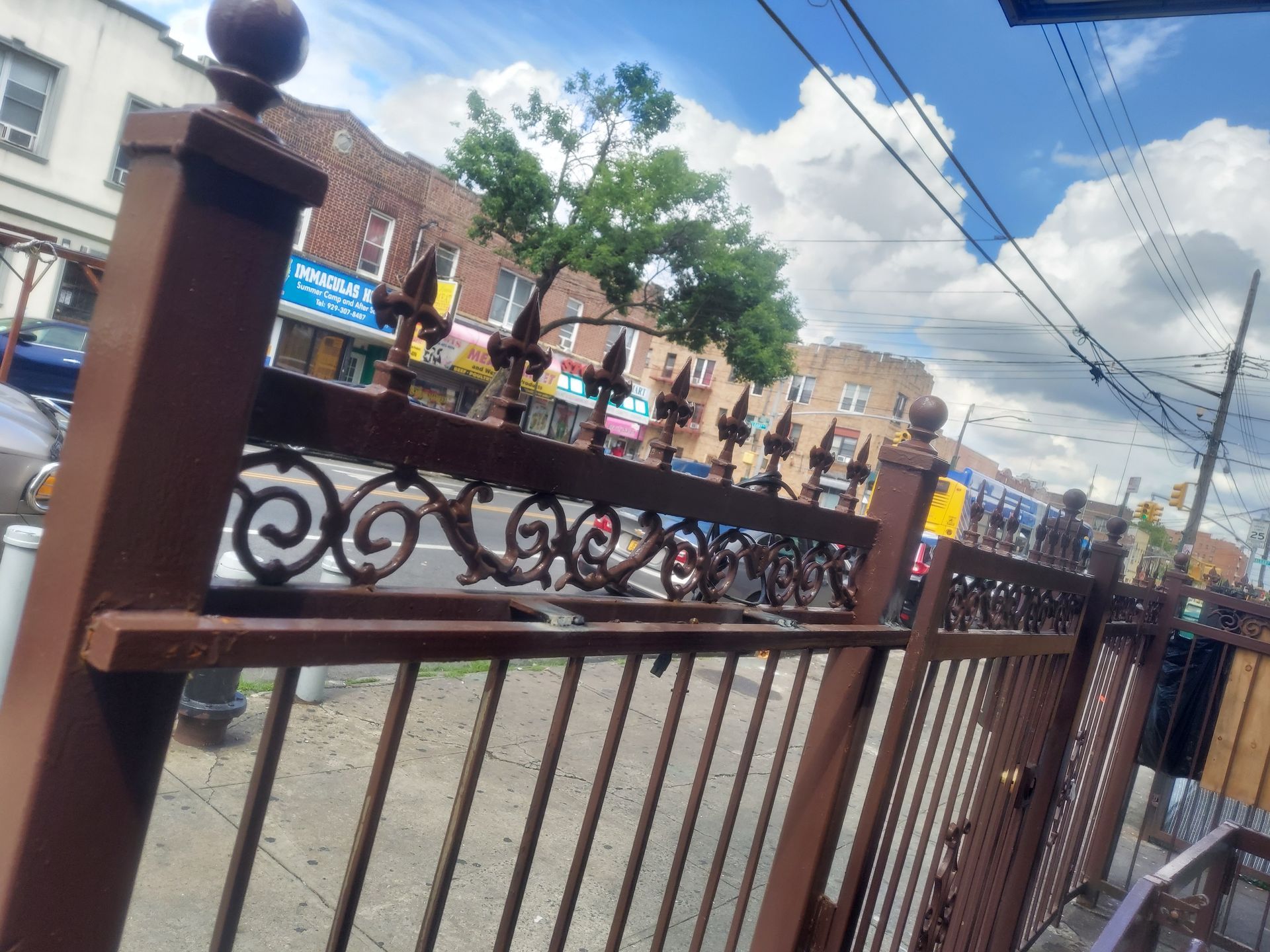 Street view through a wrought-iron gate, with brick buildings, parked bicycles, and a partly cloudy sky.