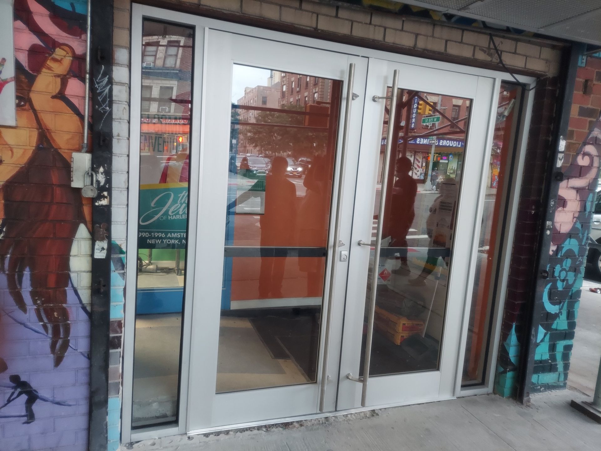 Glass storefront entrance with white double doors and colorful murals on brick walls