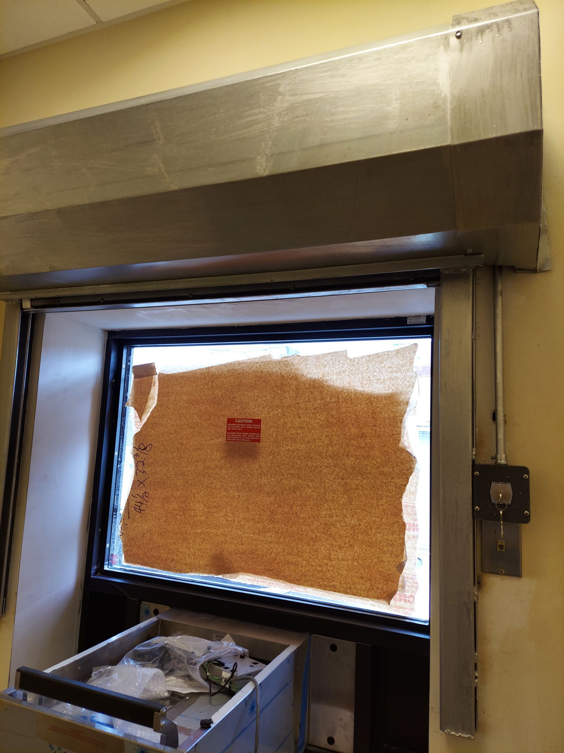 Restaurant window covered with a cardboard sign and a bin of trash below it