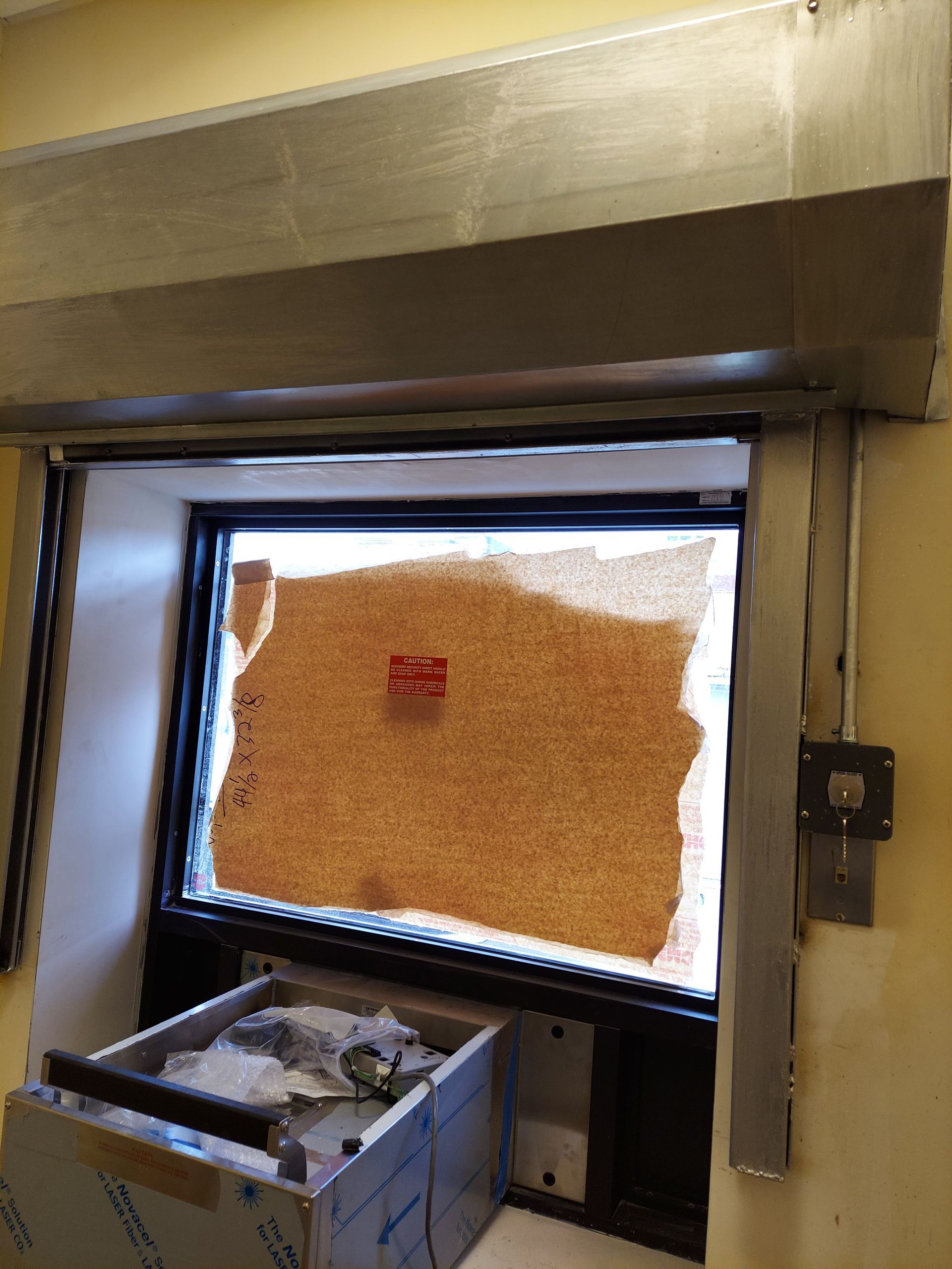 A mail slot with a metal tray and a sealed package behind a glass window.