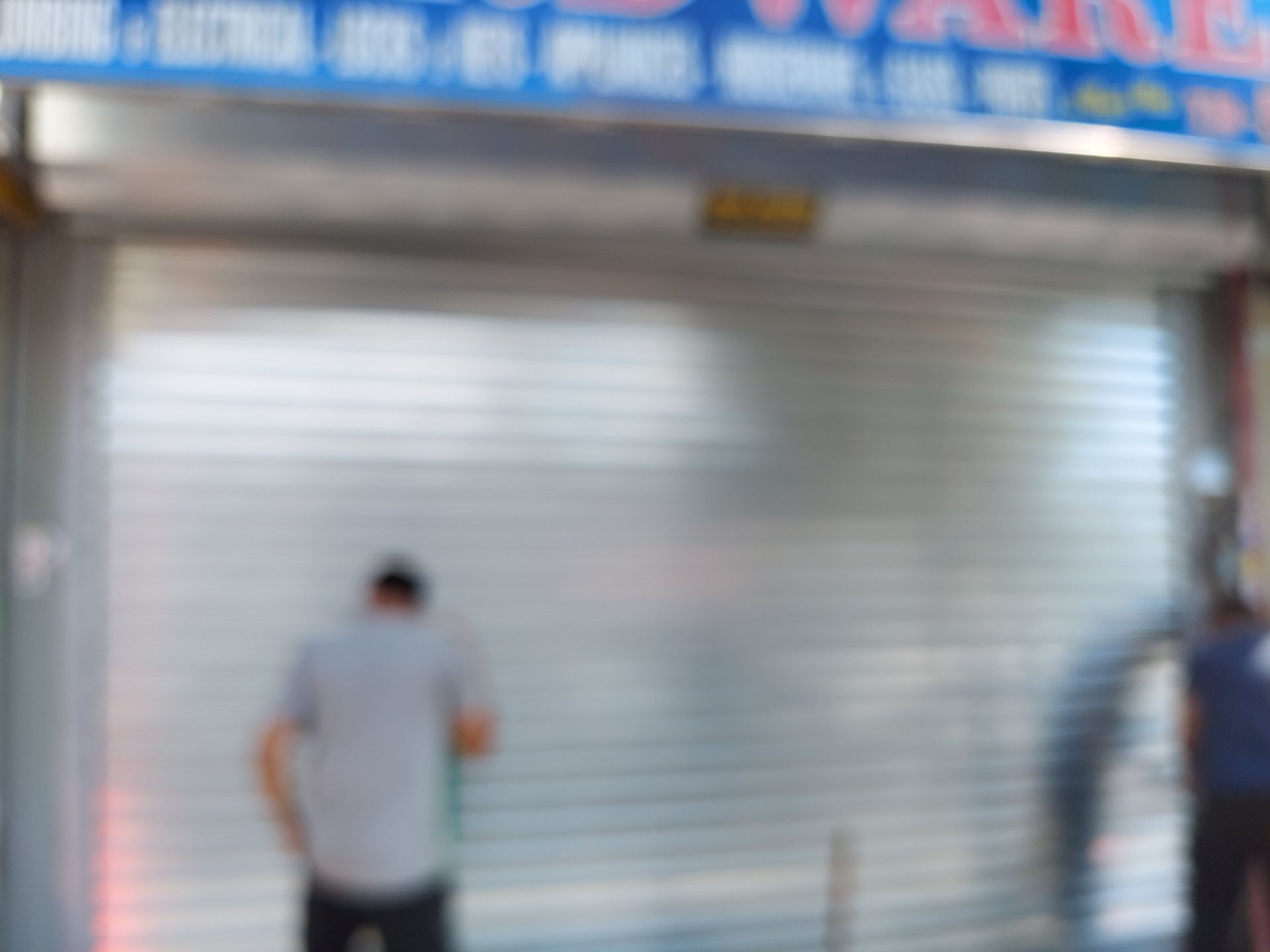 Person standing before a closed gray storefront shutter with a blue sign above.