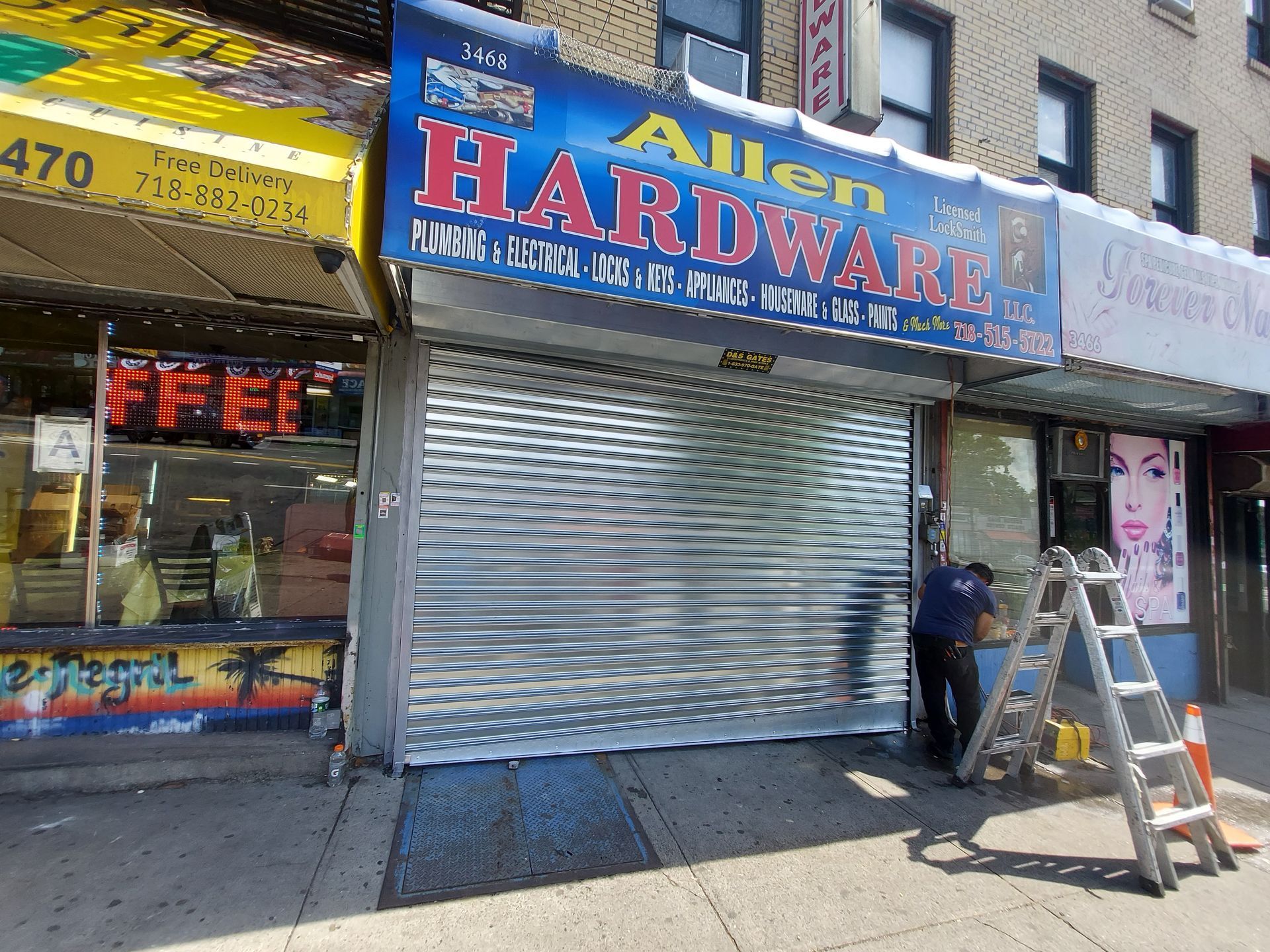 Hardware store storefront with metal shutter closed and a worker on a ladder beside it